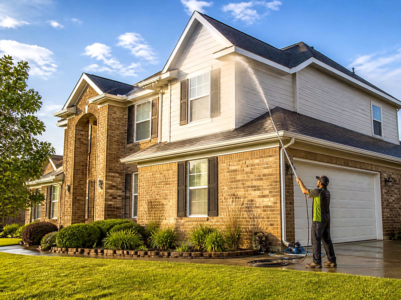 Technician house washing the siding and brick of a two-story Houston home on a sunny day